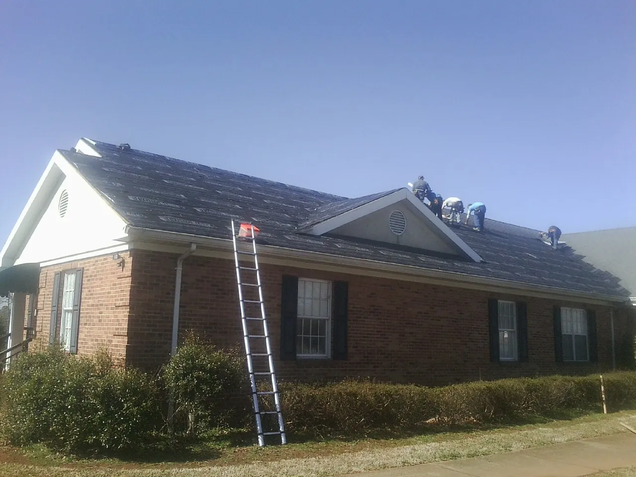 Crew tearing shingles off a brick ranch roof with a ladder set — Emergency Roof Repair work by our crew in North Attleboro