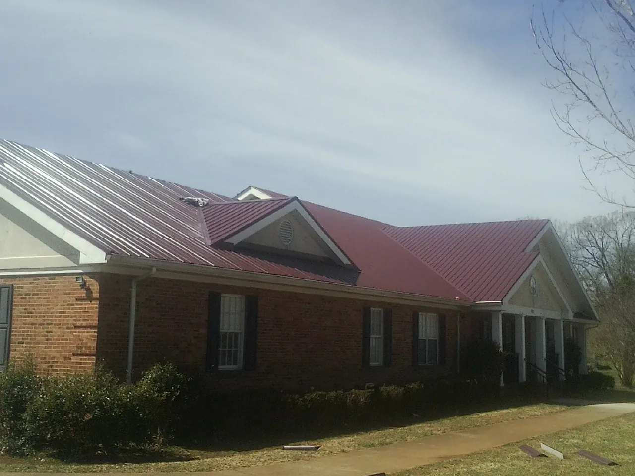 Red metal roof with gabled entries on a long brick building, from a Hail Damage Roof Repair job in North Attleboro