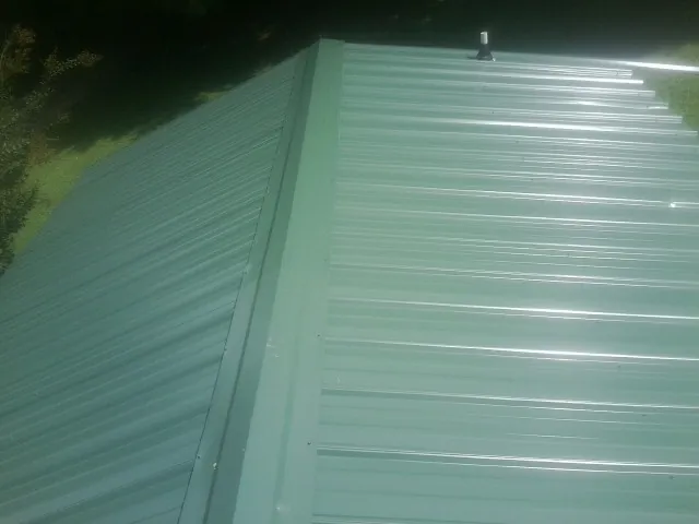 New green metal panels meeting at the ridge of a roof — Flat Roof Repair work by our crew in North Attleboro