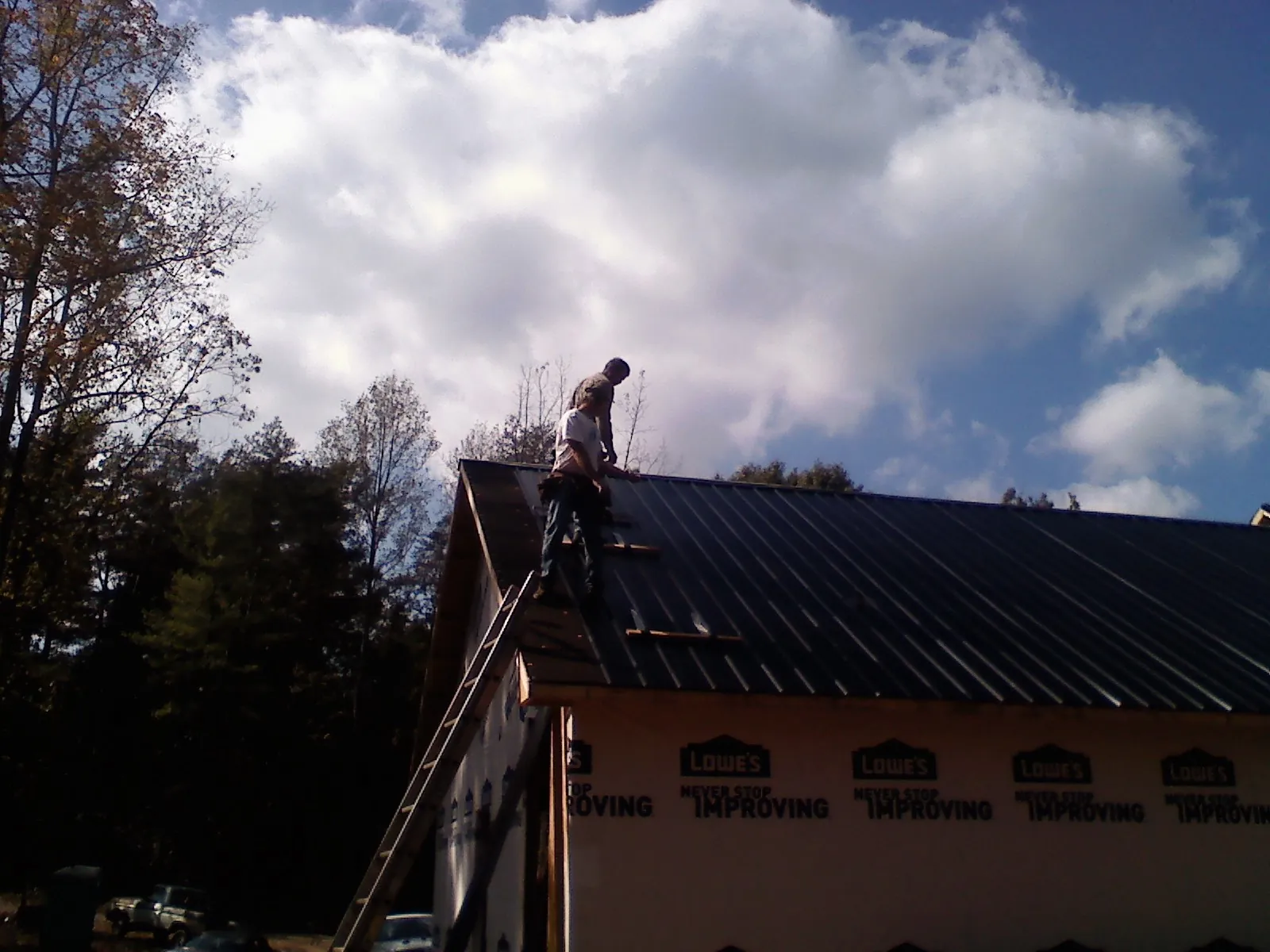 Roofer fastening dark metal panels high against a cloudy sky, from a Roof Inspection job in North Attleboro