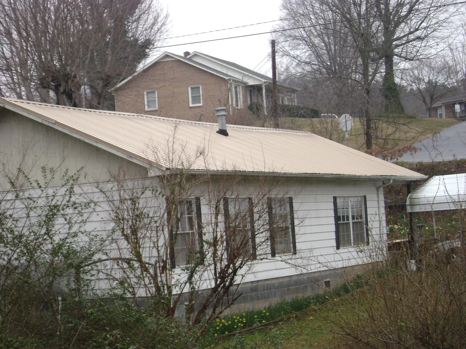 Tan metal roof on a white sided house set into a hillside — Commercial Roofing by Roofing Brothers in North Attleboro